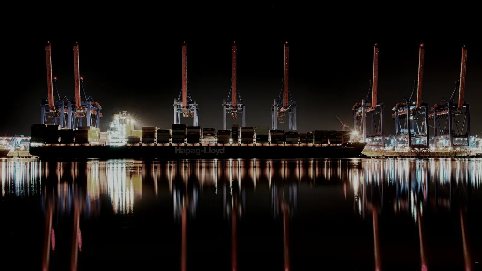 A container terminal at night, cranes lit above still black water